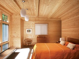 A tastefully spare selection of vintage pieces accents the warm knotty pine in the master bedroom. The orientation of the room maximizes the picture window that replaced the original garage door. Campbell designed a closet in an alcove behind the wall at the head of the bed.