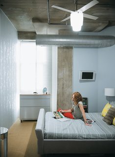 In the adjacent bedroom, decorative touches like the silver wallpaper and mirrored regency-style side table juxtapose with the exposed concrete and duct work.