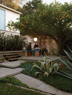 How Good Idea Studio Revamped a 1924 Clapboard House on a $62,000 Budget - Photo 3 of 11 - Surrounded by flax, agaves, and a prolific lemon tree, the gravel terrace out front makes an inviting place to eat, work, or party. Molina and Turin fashioned the table from repurposed glass and Unistrut tube steel and the humble chairs from plywood wrapped in sheets of blue foam.