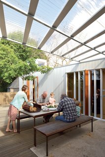 The family shares an alfresco lunch with Ikimau Ikimau, a friendly neighbor who helped build the house. The aluminum weatherboard cladding was custom-designed by O’Sullivan.