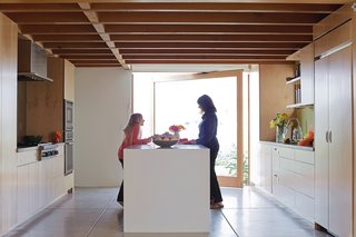 Coast Docs - Photo 7 of 13 - Carole and granddaughter Allison—–silhouetted against a glass door that pivots open to the front garden—–plot how they’ll prepare the family’s next meal at the kitchen island.