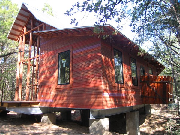 The structure was built onto a concrete-and-steel base. At left is the porch, pre-screening; at right is a cantilevered outdoor shower off the bathroom. The exterior cladding is cedar, stained in four different colors then placed randomly “for a different palette of colors, like a blend of bricks,” says Panton. “The owner’s favorite color is purple, so we added a purple board here and there.” Photo 4 of Texas Bunkhouse modern home