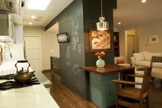 The Barn and the Lantern - Photo 3 of 9 - Architectural designers Chinmaya Misra and Apurva Pande retained the existing structural fireplace wall inside, now sheathed in useful chalkboard paneling, then knocked down a light-blocking wall between the living area and the kitchen and introduced new millwork and appliances to the space. The door at left leads to the garage; at right is the door to the couple’s former bedroom.