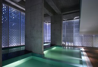 An interplay of geometries in what Khanna calls "the belly of the building." Uplights create new angles of light, raw concrete retains a rough edge and square pool tiles add texture and color while offsetting the perforated circles. The dropped ceiling at right is part of a small balcony overlooking the pools; beneath it is a sitting area.