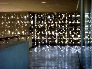The Stealth Winery - Photo 5 of 9 - Herzog + de Meuron used a variety of industrial materials throughout the structure. After ascending the stairwell to the second level, one is met by a Brutalist concrete floors, a wire-mesh ceiling, floor-to ceiling glass used for interior walls, and sunlight shining through the gabions. A varnished wood handrail contrasts the metals, stone, and glass, adding warmth to the otherwise cool setting.