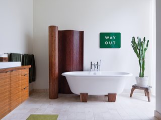 The master bathroom has a bamboo screen and a Deauville tub by Victoria + Albert. A vintage enameled metal sign from the London Underground is framed by the screen and a cactus that sits atop an African stool.