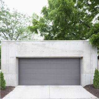 The darker gray garage door offers a chromatic and textural contrast to the concrete shell.