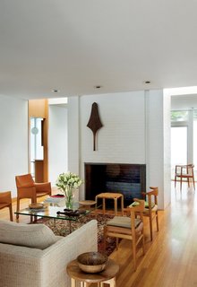 A club from the Fiji islands is mounted on the wall of the fireplace that divides the living and dining rooms. The dining room—furnished with two Cab chairs by Mario Bellini for Cassina, a pair of Cowhorn chairs by Hans J. Wegner for Johannes Hansen, the Barcelona Table by Mies van der Rohe for Knoll, and a Y61 stool by Alvar Aalto for Artek—has no windows, but lightwells on either side of the chimney provide brightness. Another design by Wegner, the Chair, peeks out from the dining room.