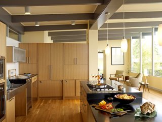 The kitchen cabinet wall provides storage and workspace, yet retains an open feel by stopping well beneath the ceiling. Sliding cabinets at the bottom reduce the number of space-hogging swinging cabinet doors, and a KitchenAid mixer is hidden behind the horizontal lift-up cabinet at right, which recesses into the wall. "The cooktop is at a height where I can see into my pot of spaghetti sauce," says Braitmayer. "I cook in this kitchen more than ever before." The countertops are heat-resistant, allowing more options for the person cooking. To the right of the sink is an ADA-compliant dishwasher from Miele. The pendant lights are from Progress Lighting.