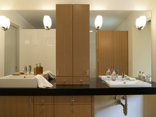The master bathroom has complementary his-and-hers sinks from Duravit, and Cifial faucets. Reflected in her mirror is a cabinet with a larger, full-length mirror inside.