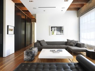 The open plan, high ceilings, and white walls all amplify the light that streams into the living room, accented with a Barcelona Couch by Mies van der Rohe for Knoll and two Blythe Pony Cube ottomans by Gus Design.