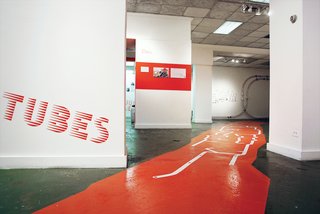 The exhibition graphics employ a customized headline typeface developed by Project Projects. The painted floor graphic shows the shape of Roosevelt Island (in orange) and the extent of the pneumatic tube system (in white).