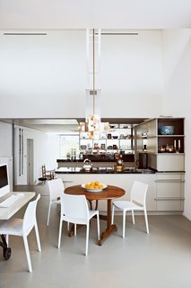 The kitchen frames a natural division between the public and private spaces of the house. The couple's private dining area features a round wooden table by Frank Bolink, and white chairs that are from Hema, a low-cost Dutch retailer.