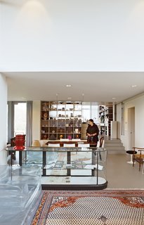 A view from the main entrance, looking toward the kitchen, reveals part of the public space of the house. Blans bought the vintage glass display case from a retailer. Behind it, the early 20th-century Amsterdam school dining table, formerly her grandmother's, has been carefully restored. The stairs lead to the builder's lift, kitchen, and the couple's private living and work area.