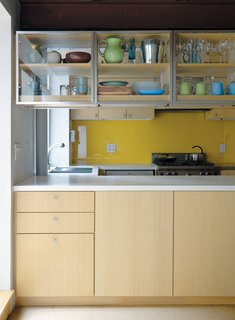 Family Home Renovation in Brooklyn - Photo 7 of 28 - Lange’s collection of vintage Heath cups and saucers, Jasper Morrison White Moon dinnerware for Rosenthal, and Simon Pearce handblown goblets fill the overhead kitchen cabinets, which are accessible from either side of the counter. The yellow backsplash is back-painted glass.