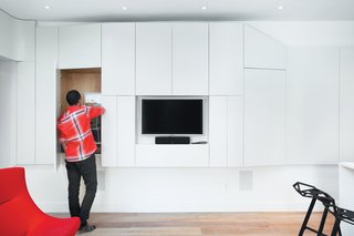 On the opposite side of the hallway, the storage wall bumps out to accommodate the television and entertainment systems and gains some hidden extra space from the former lot-line window niches.