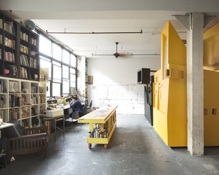 Communal Living on a Budget in Brooklyn - Photo 4 of 13 - The five roommates share the common space in their high-ceiling loft. There’s a large library and a studio. The large worktable gives Dreitlein and Ionescu, who together have a small art/architecture practice called The Objectionists, space to paint and make models.