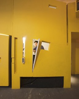 Communal Living on a Budget in Brooklyn - Photo 7 of 13 - A jumble of windows framed into the bright yellow oriented strand board (OSB) wall looks out from Ionescu’s room onto the common kitchen area. Although the team worked hard to create privacy, each room has some kind of portal or opening that connects it back to the larger loft space.