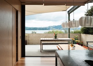 The north-facing doors slide completely away to open the house to the outdoors, offering an uninterrupted view of the water. The pendant lights over the table are from Iko Iko.