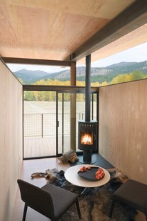 10 Cozy Spaces and 15 Products to Help You Get Ready For Fall - Photo 2 of 10 - A compact interior with a black fireplace feels simultaneously cozy and boundless, with floor-to-ceiling glass doors that open out to views of the mountains of Washington state. The cork flooring, weathered steel, and wood walls contrast with the raised, open ceiling for the perfect mix of warm and minimalist, open and enclosed.