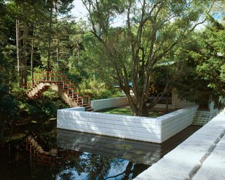 A geometric bridge connects one of the many outdoor terraces of the Dow Home to green space on the other side of the pond.