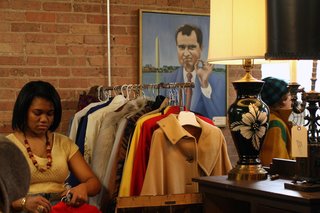 TVB is a-ok! A goofy portrait of President Nixon from Manly Vintage’s booth keeps an eye on Jillian Knox of JJoules Vintage as she stocks a rack with fab vintage coats. <br><br>Photo by <br><br>Steven Pate