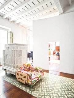 Paths of Andalusian tile and intervening plaster walls help to delineate space in the expansive apartment, which is centered around an internal entry courtyard. The armchair, designed by Peter and Alison Smithson, is covered in a Josef Frank textile from Just Scandinavian. The white piece just behind it is a repurposed Austrian stove that’s now used as a storage device.