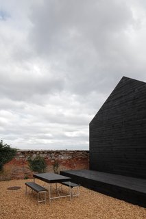 A Pair of English Barns Hide Unabashedly Bold and Budget-Friendly Minimalist Interiors - Photo 7 of 14 - A picnic table in a matching hue to the Stealth Barn rests between the two structures.