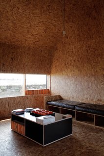 A Pair of English Barns Hide Unabashedly Bold and Budget-Friendly Minimalist Interiors - Photo 9 of 14 - A row of Penguin Classics in the window casts an orange glow on the Stealth Barn's small OSB-clad living room outfitted with more custom furniture from Turner.