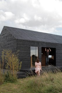 30 All-Black Exterior Modern Homes - Photo 16 of 30 - Carl Turner and Mary Martin pose on the porch of the Stealth Barn, a multipurpose structure that plays as a guest cottage, office space, and escape from whatever may be cooking at Ochre Barn.