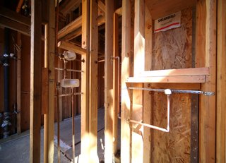 This is the master shower showing copper pipes running to shower heads and controls. The white plastic covers protect the TOTO shower control valves. Once the shower walls are completed the finished controls will be installed.