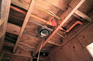This ceiling image shows a full array of infrastructure; electrical wiring, orange fire sprinkler pipes, black cast iron plumbing, and also a recessed light housing from Lumens.com.