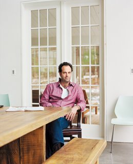 Tom Givone sits at a table of his own design, which he had fabricated from reclaimed wood by a local carpenter.