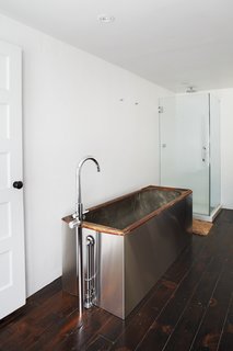 A salvaged 19th-century soaking tub wrapped in stainless steel is topped by Hudson Reed faucets.