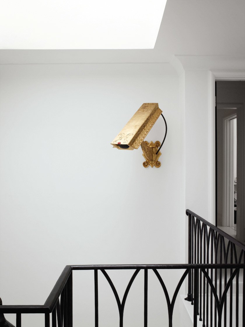 The gold (nonfunctioning) surveillance camera by artist Camp Bosworth in the stairwell previously hung in the glass entryway of the family?s former house in Houston.