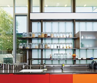 This House Doesn't Hold Back on Colorful Details - Photo 6 of 11 - The red- and orange-painted cabinets are meant to reflect sunlight and represent the heart of the home. The glass-fronted cabinets in the kitchen are by Henrybuilt, and the clear containers with dry goods are from the Container Store.