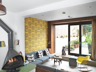 Sitting Pretty<br><br>The ground floor was originally two rooms; now it’s been transformed into one continuous space. To compensate for a low ceiling, Kiely’s team dug into the ground to create a true sunken seating section leading to the garden. Built-in sofas, an Eames rocker, a stool by G Plan, and concrete tiles outfit the space. Kiely chose a neutral charcoal finish for the Malm fireplace to balance the green linoleum floor and her own Rhododendron wallpaper in Sunflower.
