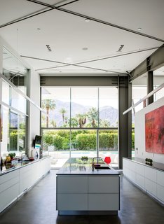 In the kitchen, which faces west to capture views of the San Jacinto Mountains, a large red work by James Jensen punctuates one wall. The induction cooktop is from Gaggenau; the sinks were sourced from Blanco.
