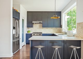 This Farmhouse-Style Home Gets a Clever and Geometric Update - Photo 3 of 5 - The kitchen sports blue-gray cabinets and Azulej tiles by Patricia Urquiola for Mutina. The Currys keep an eye on the backyard through a large Pella window, situated above a sink with a Sensate faucet from Kohler. The range is by BlueStar.