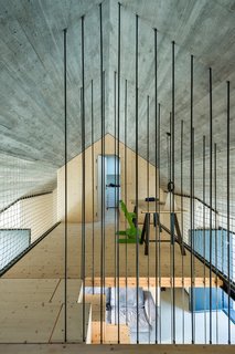 The upper level contains the master bedroom and the kids' room. "We wanted the upstairs gallery that connects the two bedrooms to be as open as possible," principal Aljosa Dekleva says. "The rope mesh works as a fence for security, but is also performs as a multifunctional transparent wall on which one can hang different objects." A desk provides an additional workspace.