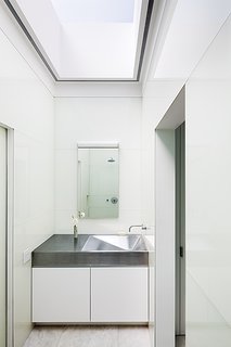 An angular brushed-stainless-steel sink and a painted plywood vanity in the third floor’s master bathroom are custom. The general contractor built the vanity and comissioned the sink from New York’s Master Restaurant Equipment. Back-painted glass panels by Bendheim clad the walls, and the fixtures are from California Faucets. Recessed lighting surrounds the perimeter of the Circle Redmont skylight, and the wall sconce over the Robern mirror is from Glashütte Limburg.