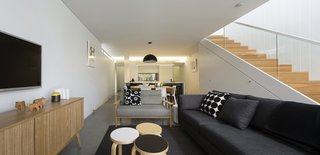 Renovation Near Sydney Opens Home Onto a Lush Garden - Photo 3 of 8 - The extension’s lower level flows uninterrupted from the garden to the kitchen. Storage units hidden under the staircase give the living spaces an uncluttered feel. A Skygarden pendant by Marcel Wanders hangs over Snow 300 dining chairs by James Richardson, providing light in those rare hours when sunlight isn’t streaming in.