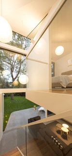 Renovation Near Sydney Opens Home Onto a Lush Garden - Photo 7 of 8 - Thanks to the extension’s vaulted ceiling, the master bedroom and minimalist staircase have views of the sky. Polly admits to having sacrificed floor area so that the full-height stairwell could achieve a stronger connection with the outdoors. Toyo Ito Mayhuma pendants hang from the ceiling, accentuating the space’s dramatic height.