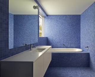 The bathrooms are tiled in bright blue mosaic to offset the home’s limited materials and color palette. The sinks, toilets, and tubs are by Villeroy & Boch, while the faucets and towel rails are by Grohe and Avenir, respectively.