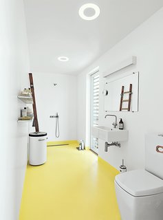 In the bathroom, the home’s epoxy floor transitions from whitish gray to submarine yellow. The sink and tub are by Galassia, and the faucets are by Vola. A ladder, which serves as a towel rack, was sourced from the Danish Emergency Management Agency. The black-and-white industrial laundry bin is by Vipp. 