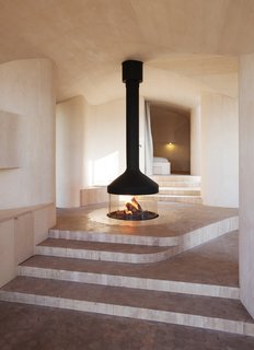 This layout revolves around a central "campfire" that burns beneath a suspended mantel. Since it’s located at the access level, the fireplace's flickering warmth can be enjoyed throughout the house. The surrounding floor is covered with hexagon tiles cut from marble, which transition into tiles made of birch log in the rest of the house.