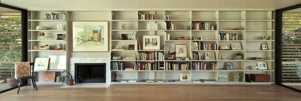 In the living room, the Brillharts created a “unified, simple and clean design” that incorporated a bookcase and fireplace along the continuous 30-foot long anchor wall. The shelves are inset several inches away from the glass walls on either side. Each individual layer cantilevers outwards to create a floating effect that mirrors the way the house itself floats above the ground. Photo 7 of Brillhart House modern home