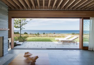 To further connect the indoor spaces with the New England landscape outside, glass walls in the living and dining areas slide open to eliminate the barriers between indoors and outdoors. Green slate tiles compose the flooring inside.