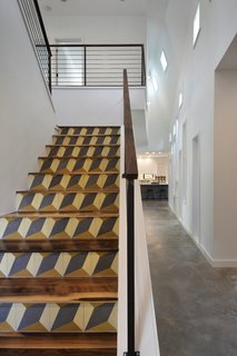 A Mighty Oak Tree Frames This Family Home in Austin - Photo 2 of 10 - An intricately detailed staircase leads to the central wing’s second level. Its walnut treads and top rail harmonize with the welded steel rod railings. The geometric pattern on the staircase’s risers comes from encaustic tiles that were handmade in Tuscaloosa, Alabama.