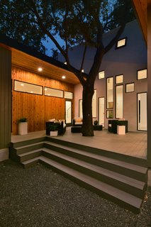 The central oak tree sprouts out of the rear deck. The atrium’s array of windows draw the eye in the tree’s direction. The wood cladding of the single-story wings provide a pleasant contrast with the central volume’s stucco finish.